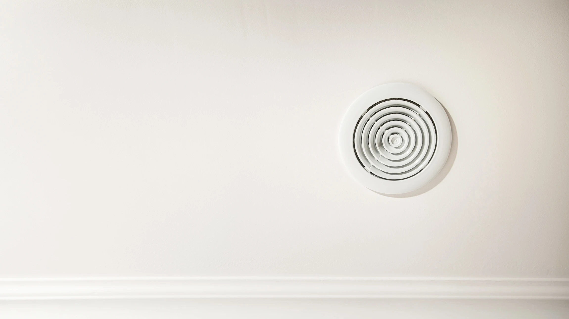 Mains installant une grille d'aération blanche dans un plafond résidentiel, accès visible au conduit de ventilation dans les combles
