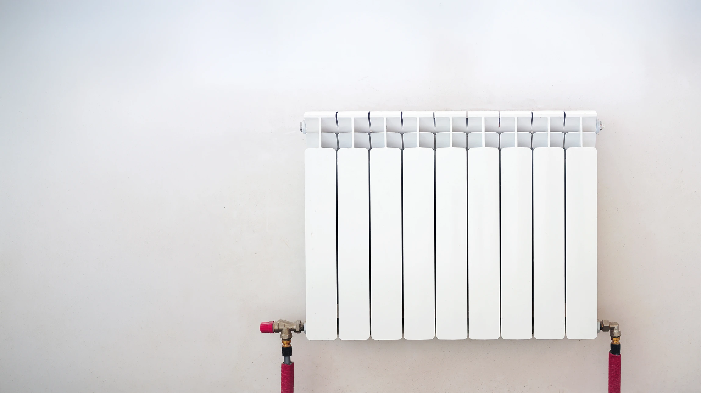 Un technicien en uniforme bleu travaille sur un radiateur mural blanc, utilisant une clé à molette pour intervenir sur la robinetterie thermostatique