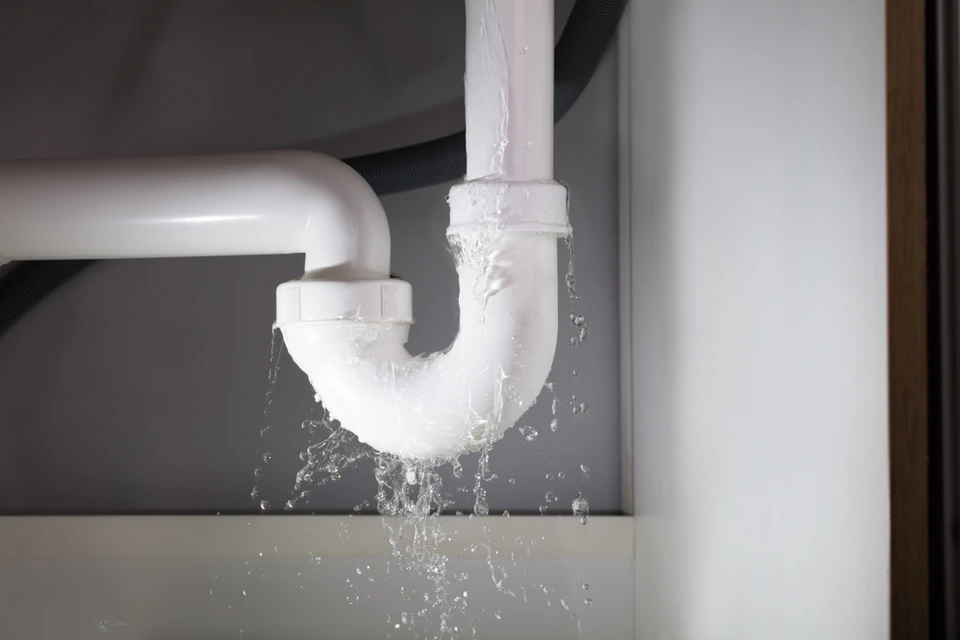 Un plombier en combinaison rouge effectue un débouchage de canalisation dans des toilettes blanches à l'aide d'un furet électrique