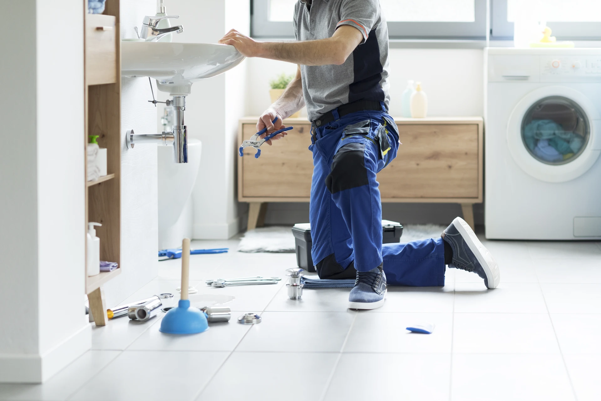 Plombier en combinaison bleue installant robinetterie de baignoire îlot dans salle de bain moderne, consultant smartphone
